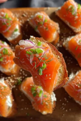 Smoked salmon crostini topped with cream cheese and herbs on a wooden platter.