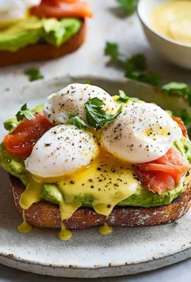 Avocado Toast topped with Eggs Benedict, garnished with herbs and served on a plate.