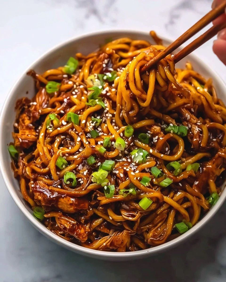 Sticky Garlic Chicken Noodles served in a bowl garnished with herbs.