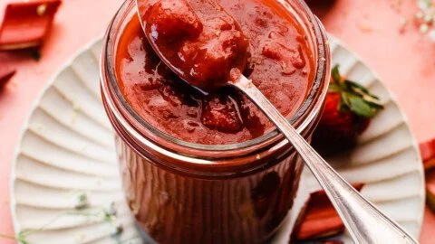 Homemade strawberry rhubarb sauce in a jar with fresh strawberries and rhubarb stalks