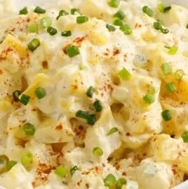 A bowl of creamy potato salad garnished with herbs and vegetables