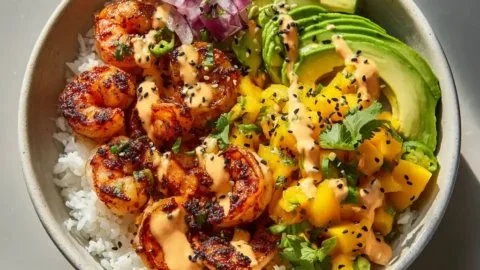 A colorful charred shrimp and avocado bowl garnished with fresh vegetables and herbs.