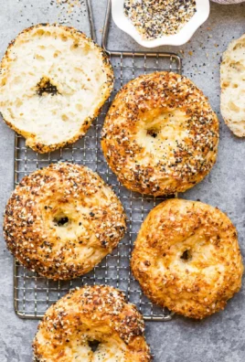 Baked protein bagels topped with cottage cheese on a wooden cutting board.