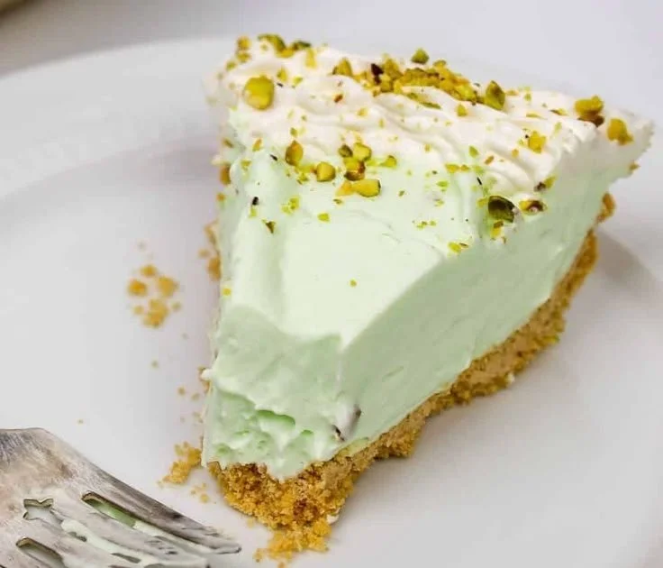Slice of cool and creamy pistachio pie topped with whipped cream and pistachios.