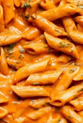 Bowl of creamy tomato pasta garnished with fresh basil and parmesan cheese.