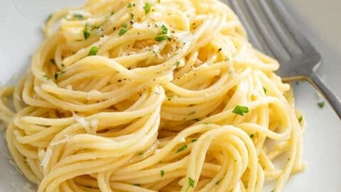 Plate of garlic buttered noodles garnished with parsley and parmesan cheese